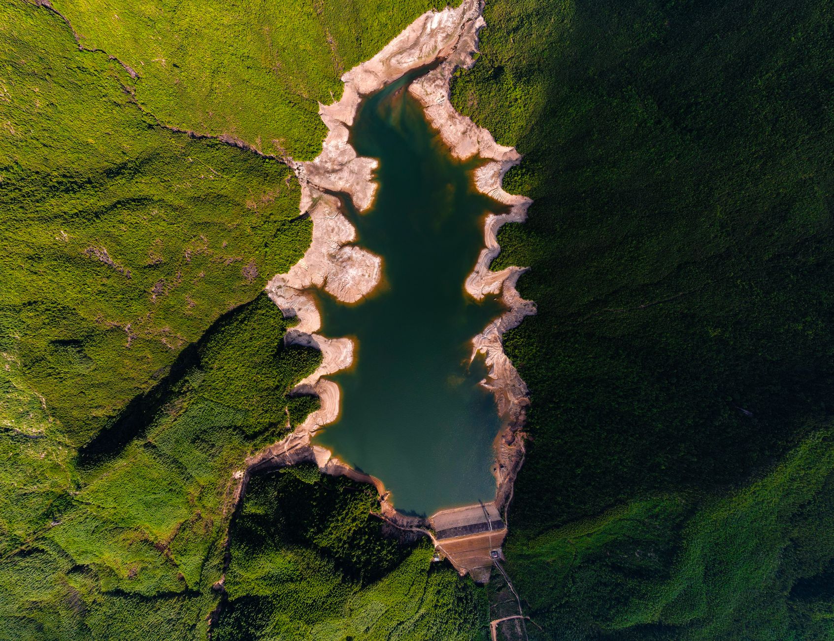 山々の中に静かに水を湛える巨大なダムと貯水池、山間部の美しい空撮風景