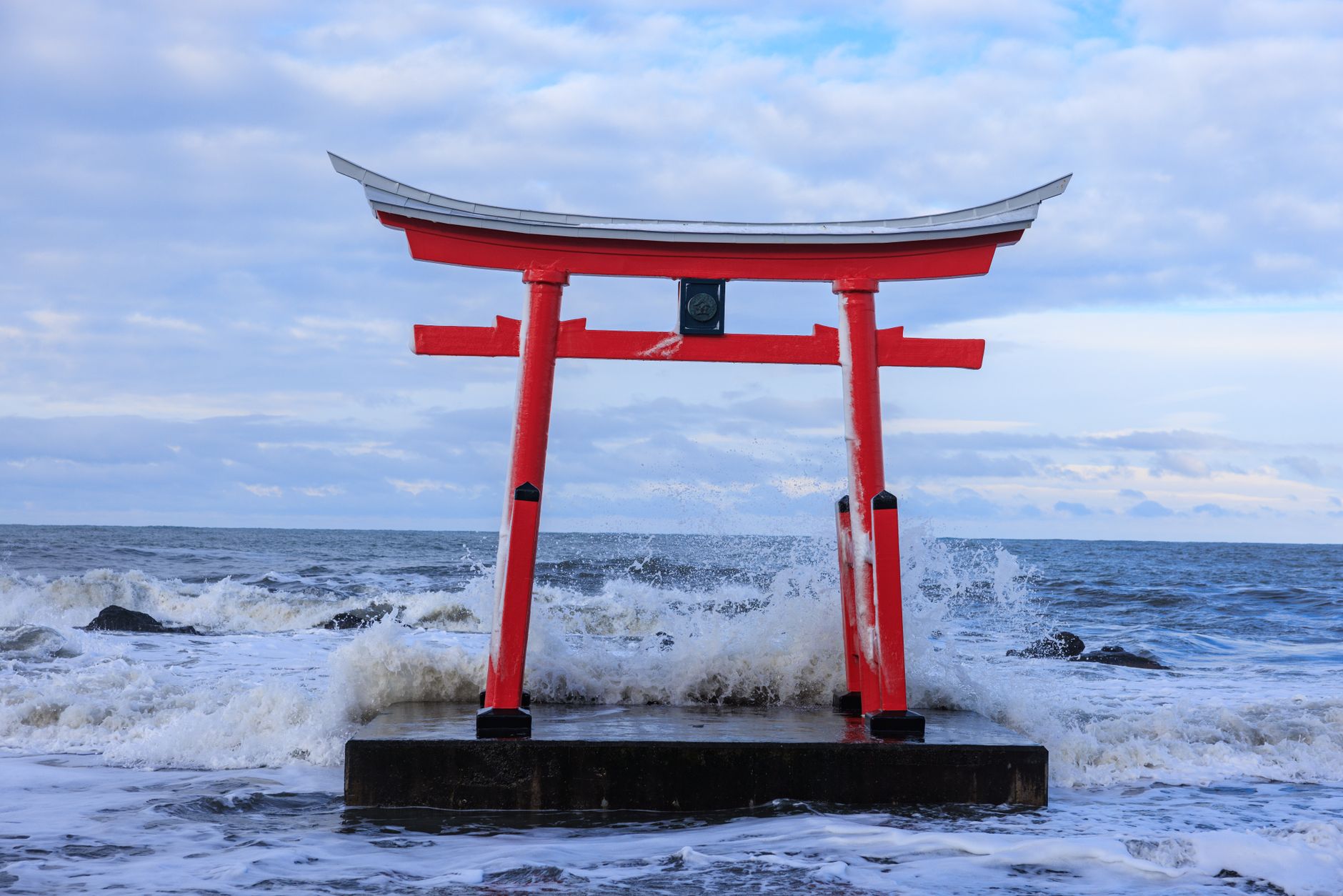 打ち寄せる波の奥に立つ海辺の赤い鳥居